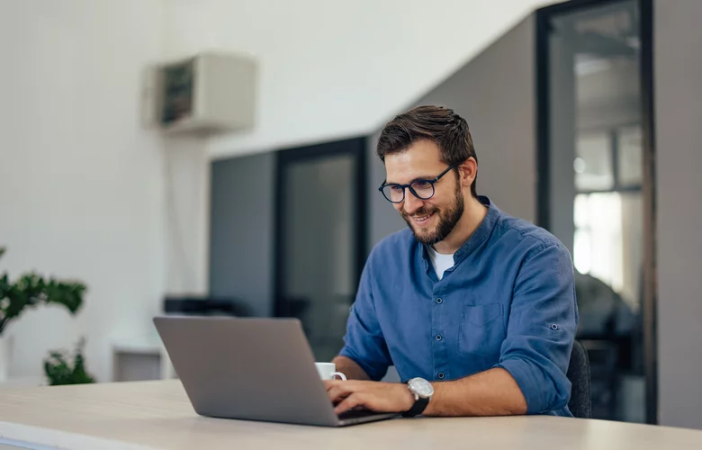 mladý muž v modrej košeli sedí za stolom a pracujem na laptope