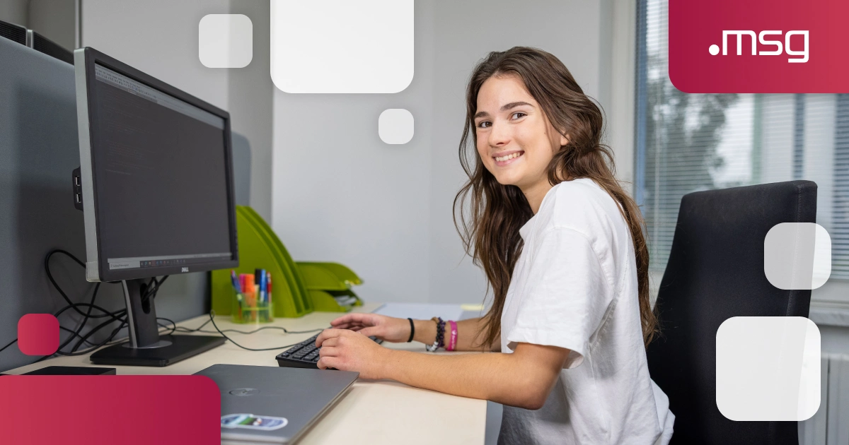 young female IT tester working at a computer and smiling at the camera in an msg office