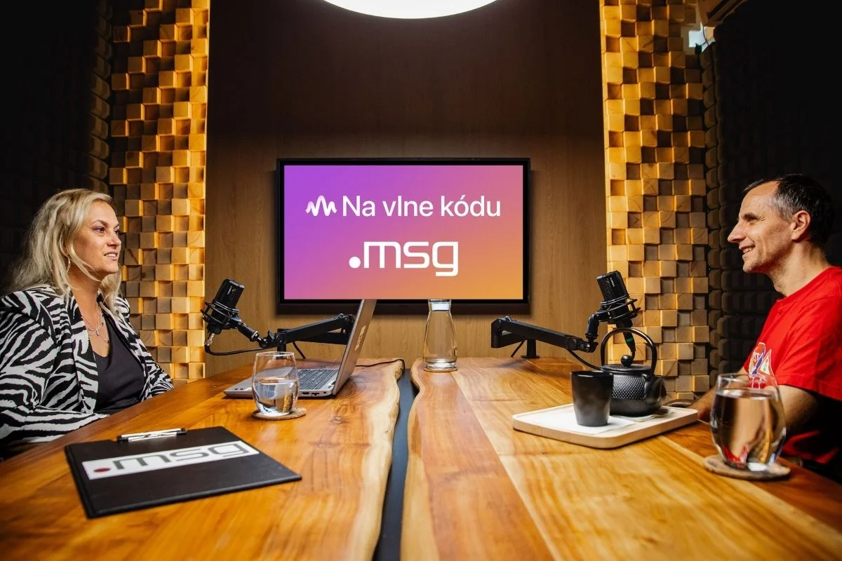 msg-podcast-na-vlne-kodu – msg life Slovakia Žena a muž sedia oproti sebe v štúdiu s mikrofónmi, za nimi svieti obrazovka s názvom podcastu Na vlne kódu.