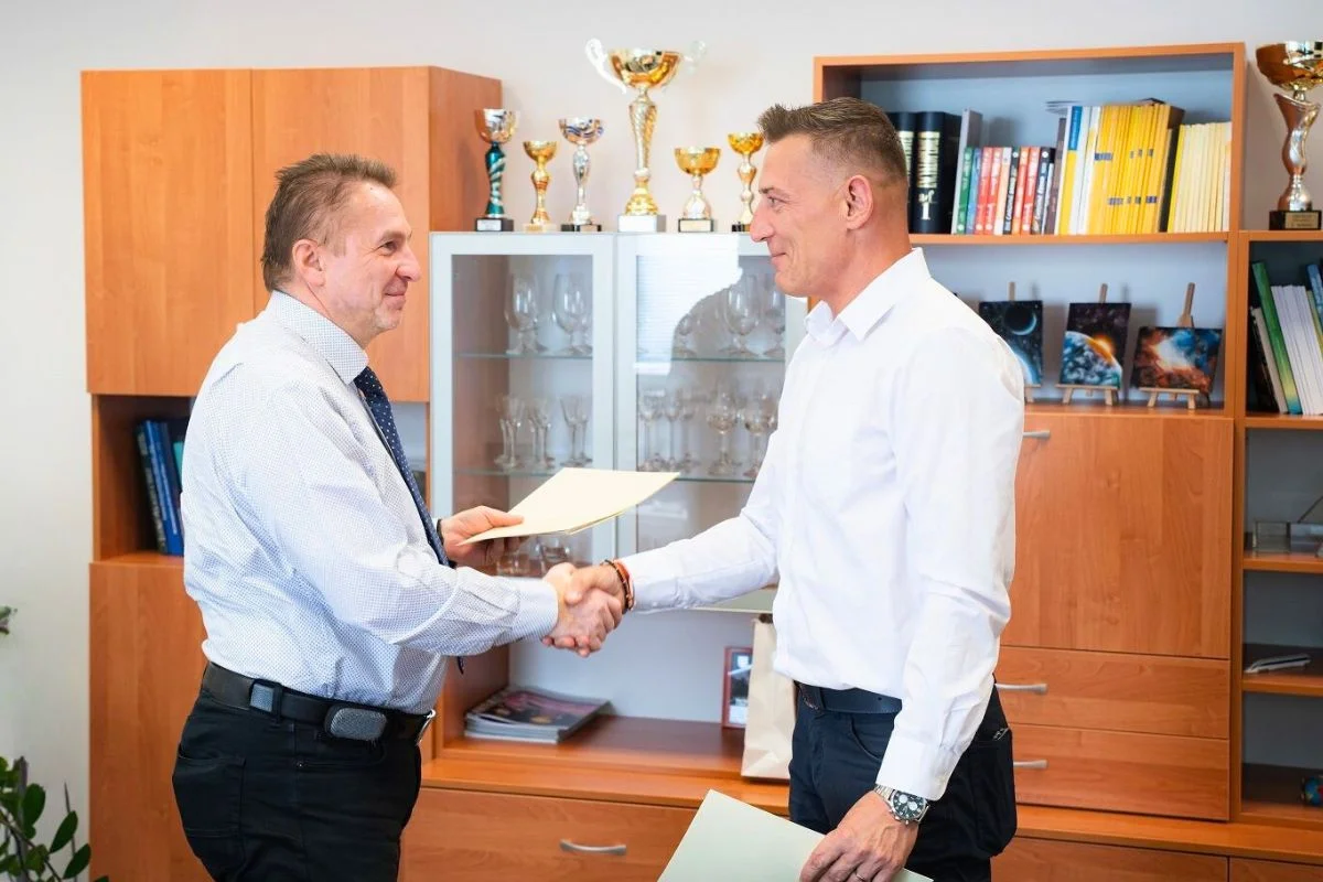 partnerstvo-msg-life-slovakia-fri-uniza – msg life Slovakia Dvaja muži v kancelárii si podávajú ruky pri podpise dokumentov, za nimi sú vitríny s trofejami.